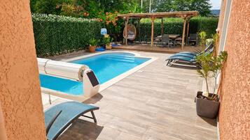 Ein Swimmingpool mit einer Holzterrasse, Liegestühlen und einer Pergola.