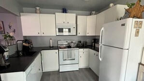 Una cocina compacta con gabinetes blancos, microondas, estufa y refrigerador.