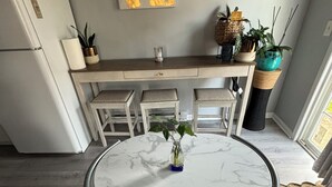 Una cocina compacta con una mesa redonda de mármol, taburetes de barra blancos y un refrigerador.