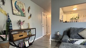 Una sala de estar con piso de madera, un tapete estampado, un sofá, una consola con objetos decorativos y una pared con obras de arte.
