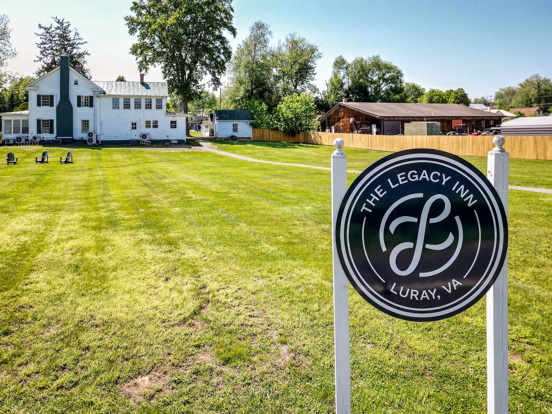 Skilt for The Legacy Inn i Luray, VA, med en velholdt græsplæne og en hvid bygning i baggrunden.