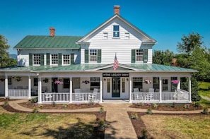 A two-story white building with a green roof, a porch with white railings, and an American flag. - 1BR suite w/ Wifi & workspace (Luray)