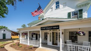 A white building with a porch, an American flag, and a sign reading 'The Legacy Inn.' - Charming suite w/ TV & patio (Luray)