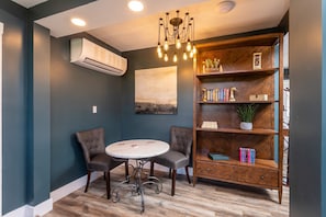 A room with a round table, two chairs, a bookshelf, and a ceiling light fixture.