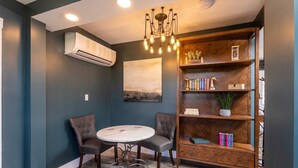 Une pièce avec une table ronde, deux chaises, une bibliothèque et un luminaire au plafond.