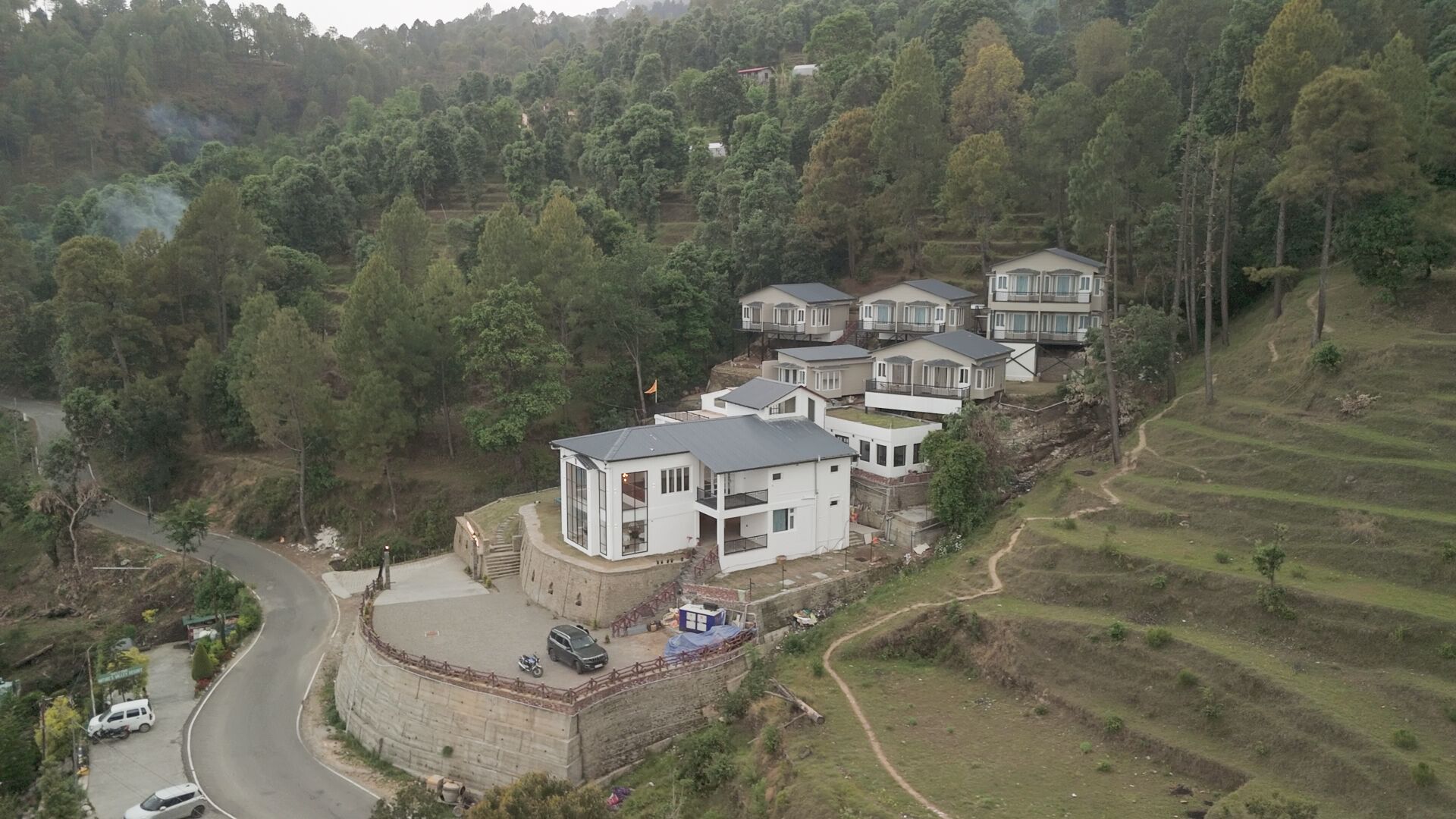 A hillside residential area with modern houses, a curved road, and terraced fields.