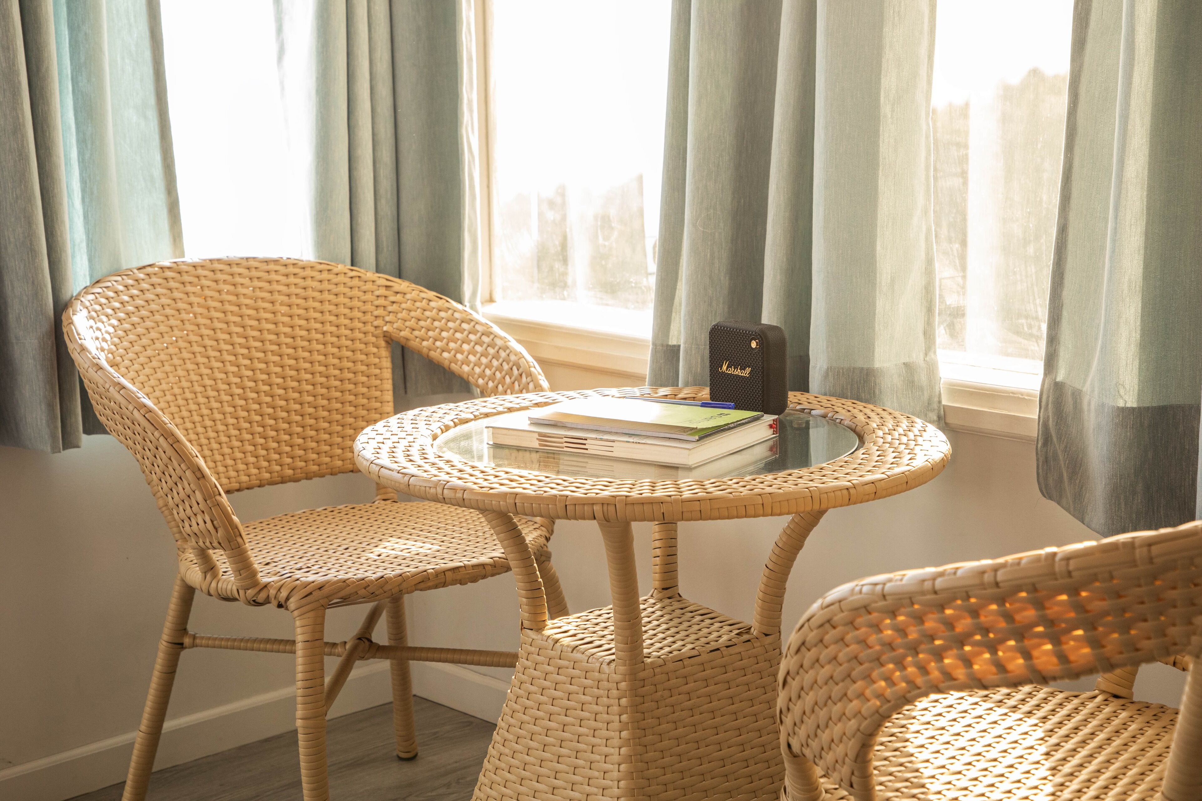 A wicker chair and table set by a window with curtains.