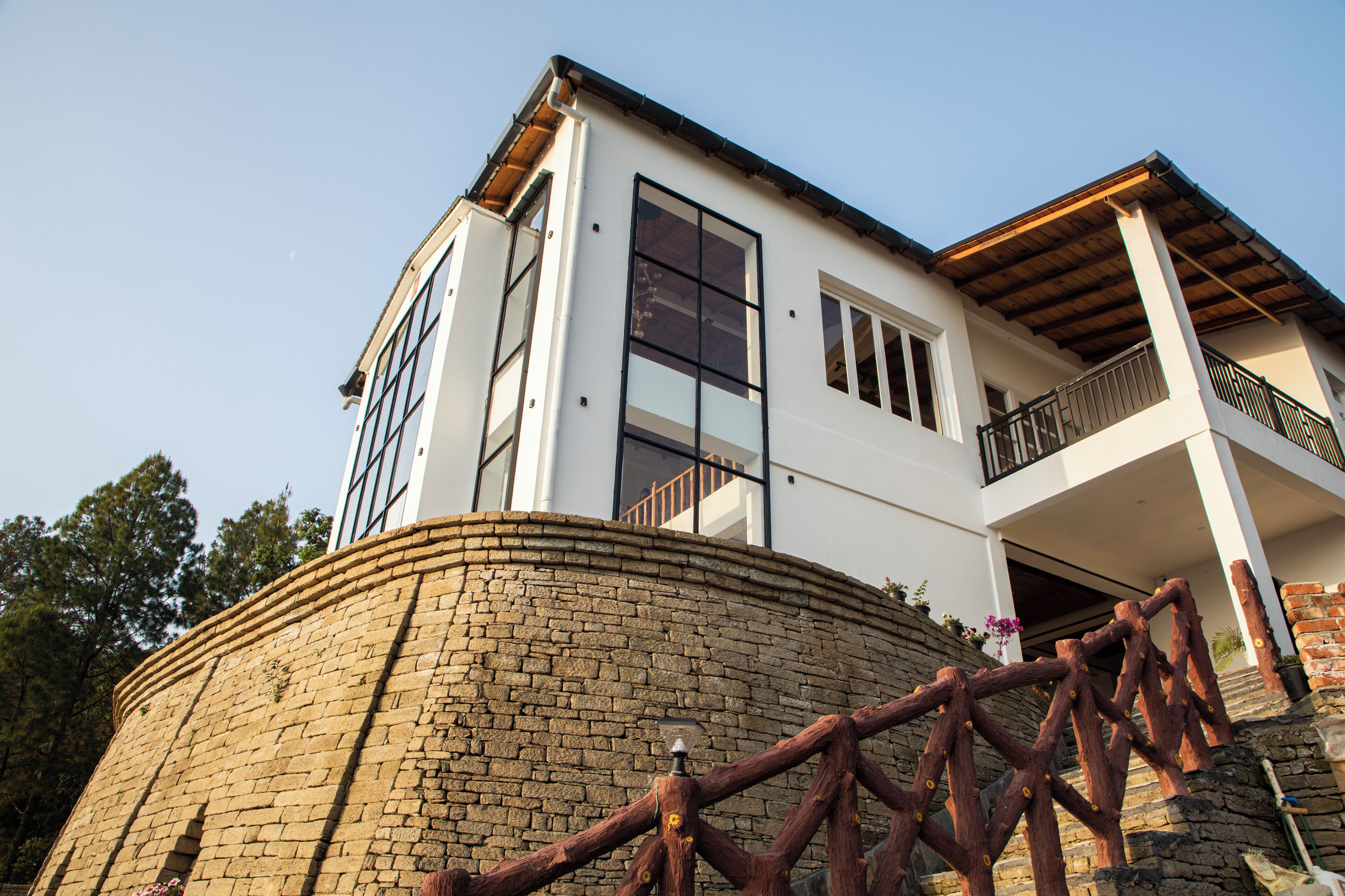 A modern two-story house with a stone retaining wall, large windows, and a balcony.