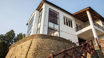 A modern two-story house with a stone retaining wall, large windows, and a balcony.