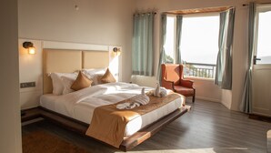 A spacious hotel room with a large bed, a comfortable chair, and a view of the outdoors through the windows. - Spellmount - Himalayan View Infinity Pool Resort In Kausani (Kausani)