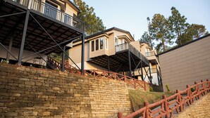 A multi-story building with a brick retaining wall and a wooden fence. - Spellmount - Himalayan View Infinity Pool Resort In Kausani (Kausani)
