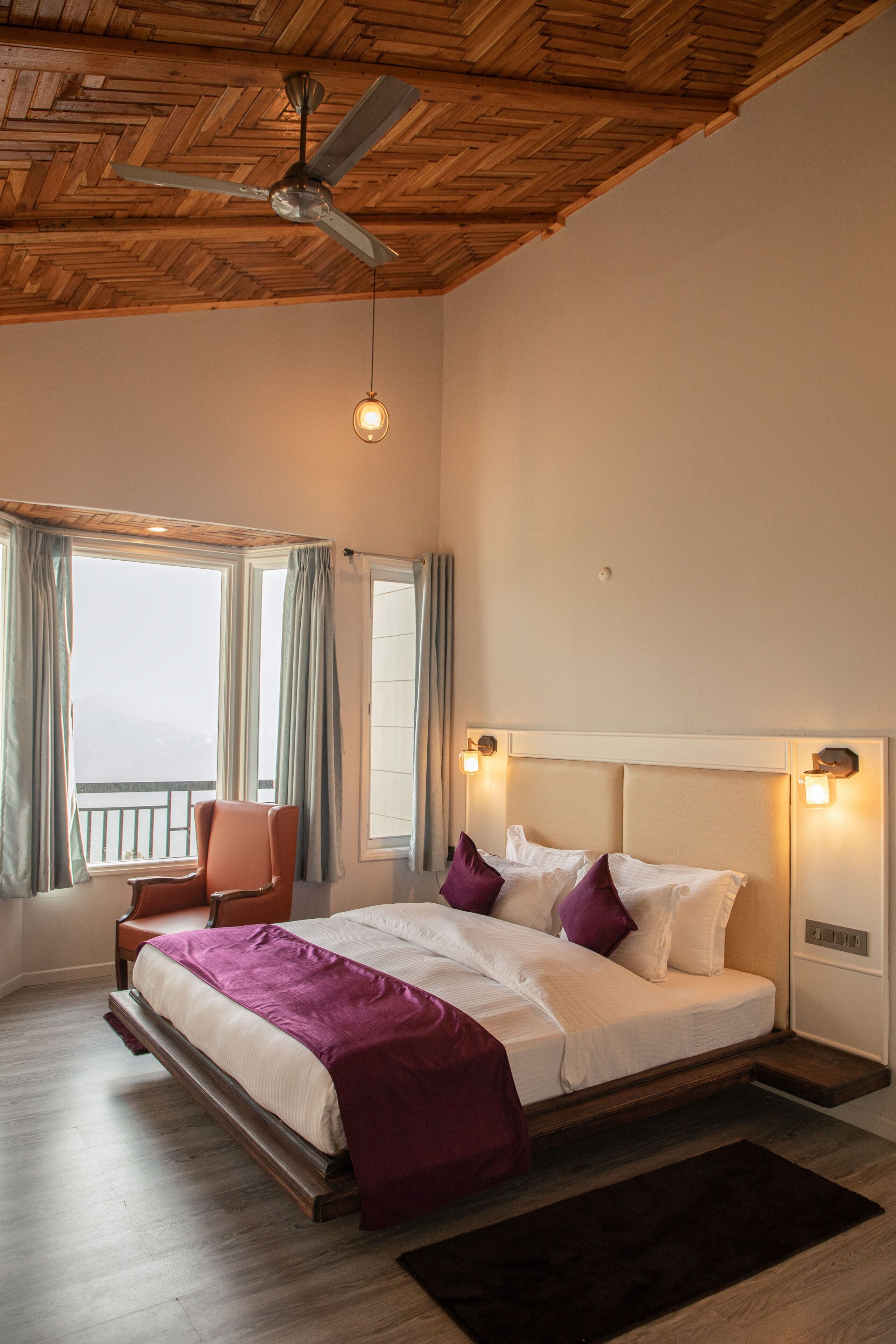 A bedroom with a bed, a chair, a ceiling fan, and a view of the outside.