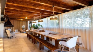 Un vaste espace dédié à la salle à manger, avec une longue table en bois, des chaises blanches et des lampes en osier suspendues au plafond.