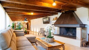 Un salon chaleureux avec un plafond en bois, une cheminée, un canapé, une table basse et un téléviseur fixé au mur.