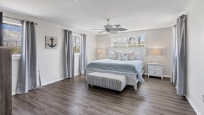 A bedroom with a bed, nightstands, a bench, a ceiling fan, and a window with curtains. - Lemon Bay Getaway - canal front leading to Lemon Bay and Stump Pass (Englewood)