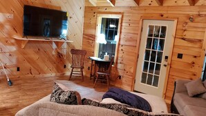 Un acogedor interior de cabaña de madera con un sofá, una mesa de comedor y un televisor montado en la pared.