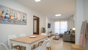 A modern living room with a wooden dining table, white chairs, a sofa, and a TV. - sibssanlúcar Camelias (Sanlucar de Barrameda)