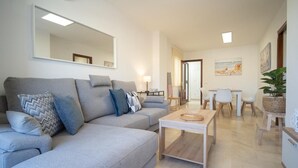 A modern living room with a grey sofa, a coffee table, and a dining area with a table and chairs. - sibssanlúcar Camelias (Sanlucar de Barrameda)