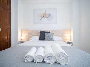 Una cama bien hecha con sábanas blancas y toallas enrolladas, un cabecero de madera y una obra de arte abstracta colgada en la pared.