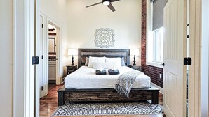 Une chambre à coucher comprenant un lit, un ventilateur de plafond, un élément décoratif mural et une fenêtre.