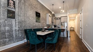 Una cocina moderna con armarios blancos, piso de madera oscura y pared de ladrillo con obras de arte.