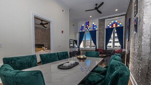 Un moderno comedor con una mesa de mármol, sillas de terciopelo verde y vistas de la ciudad a través de amplias ventanas con cortinas azules.