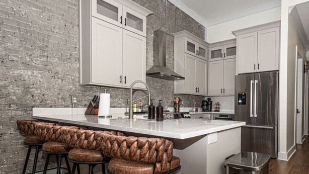 Una cocina moderna con armarios blancos, un refrigerador de acero inoxidable y una zona de bar con taburetes de cuero.