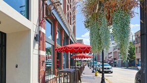 A sidewalk with outdoor seating, red umbrellas, and a brick building with a clock. - Downtown Luxury Condo | Near UT (Knoxville)