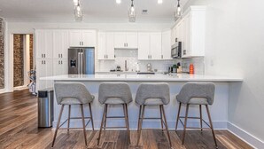 A modern kitchen with white cabinets, stainless steel appliances, and a central island with bar stools. - Downtown Luxury Condo | Near UT (Knoxville)