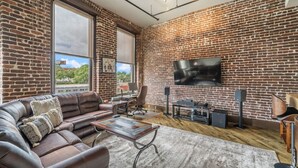 Un salon avec un mur en briques, un canapé en cuir, un téléviseur à écran plat et une table basse.