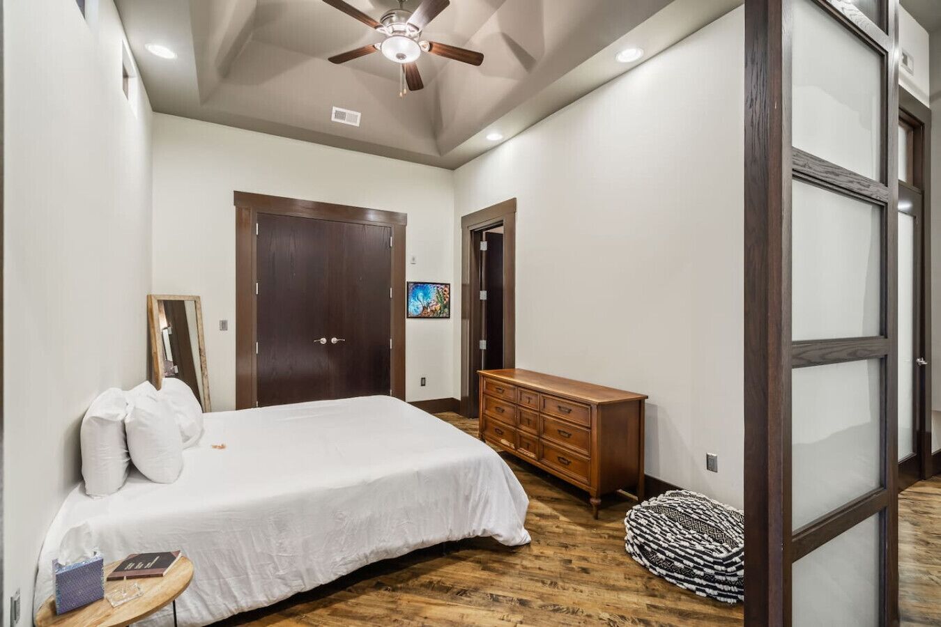 A bedroom with a bed, a wooden dresser, a ceiling fan, and a large window.