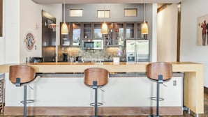 Une cuisine moderne dotée d’un îlot central, de tabourets de bar et de luminaires suspendus.