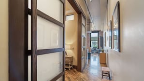 Un pasillo con suelo de madera, un escritorio y sillas, que conduce a una habitación con cama y escritorio.