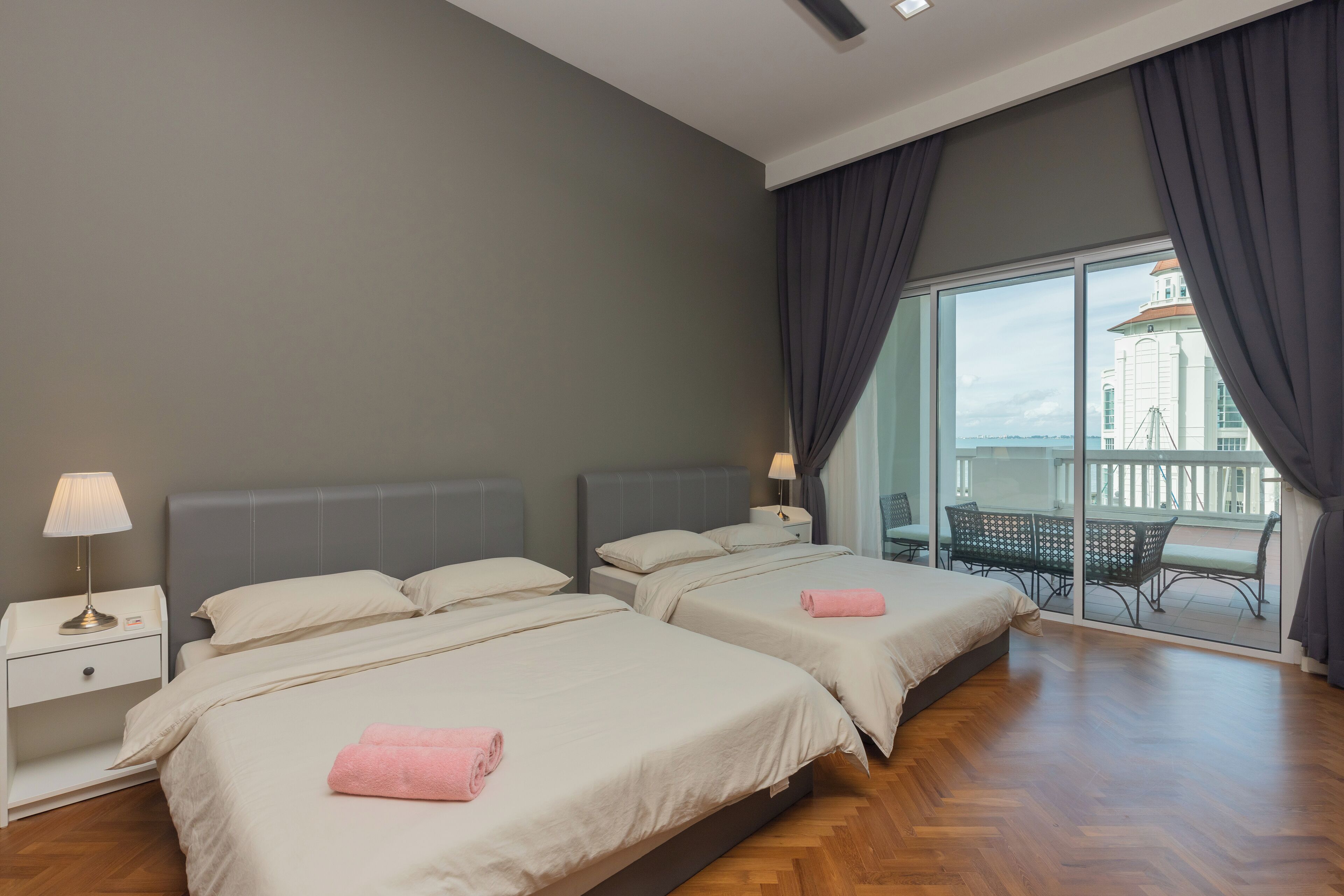 Habitación de hotel con dos camas, una mesita de noche, una lámpara y un balcón con vistas a un edificio.