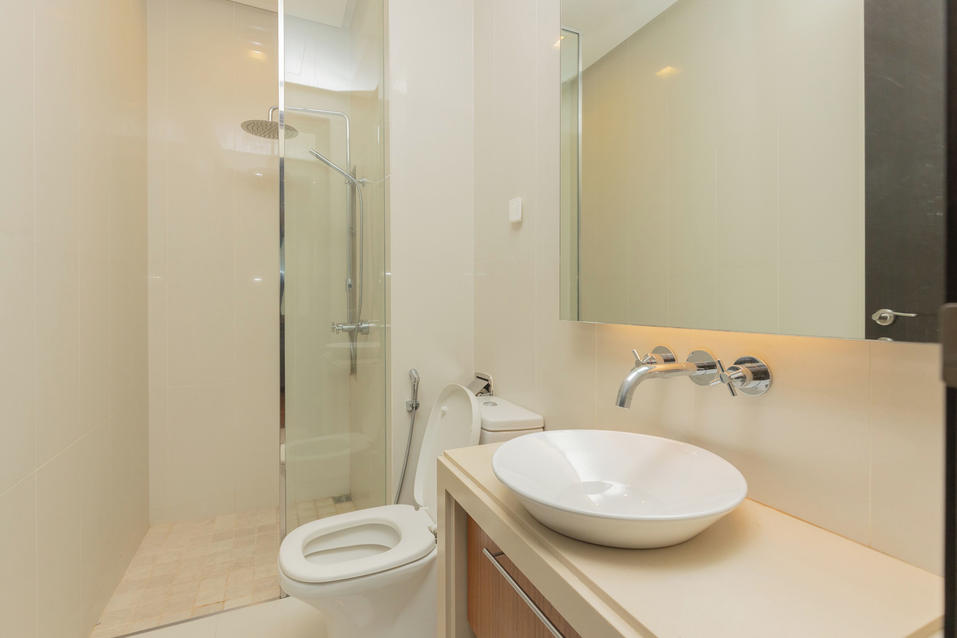 Un baño moderno con ducha envuelta en vidrio, inodoro blanco y un lavamanos grande con espejo superior.