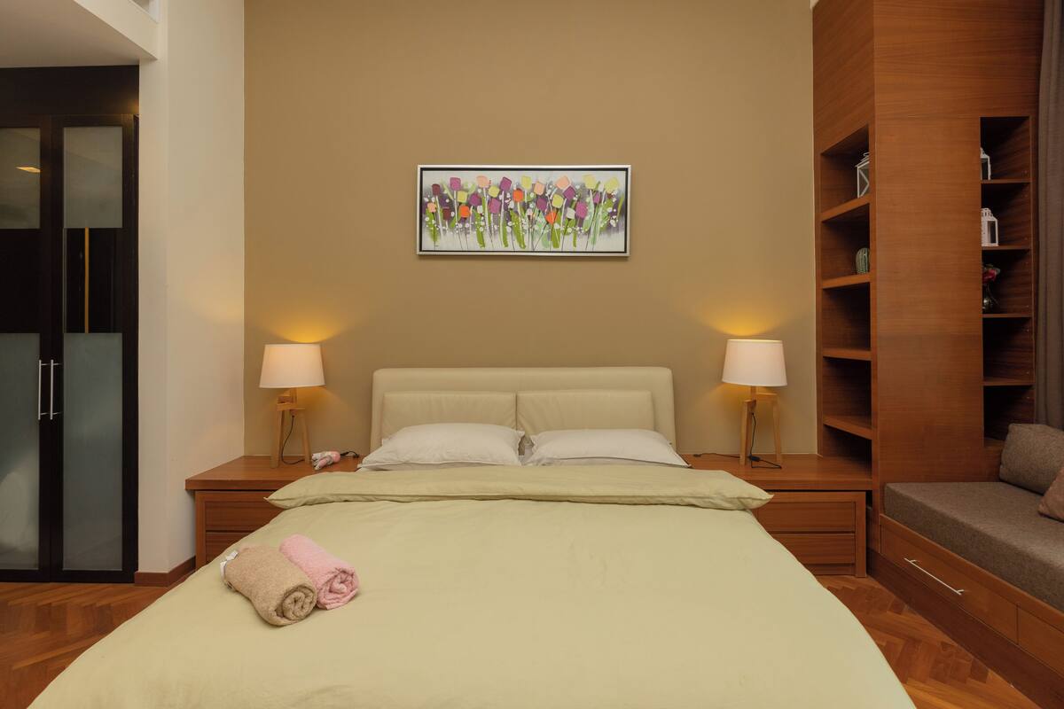Habitación de hotel con una cama, dos mesitas de noche con lámparas, un armario de madera y una obra de arte colgada en la pared.