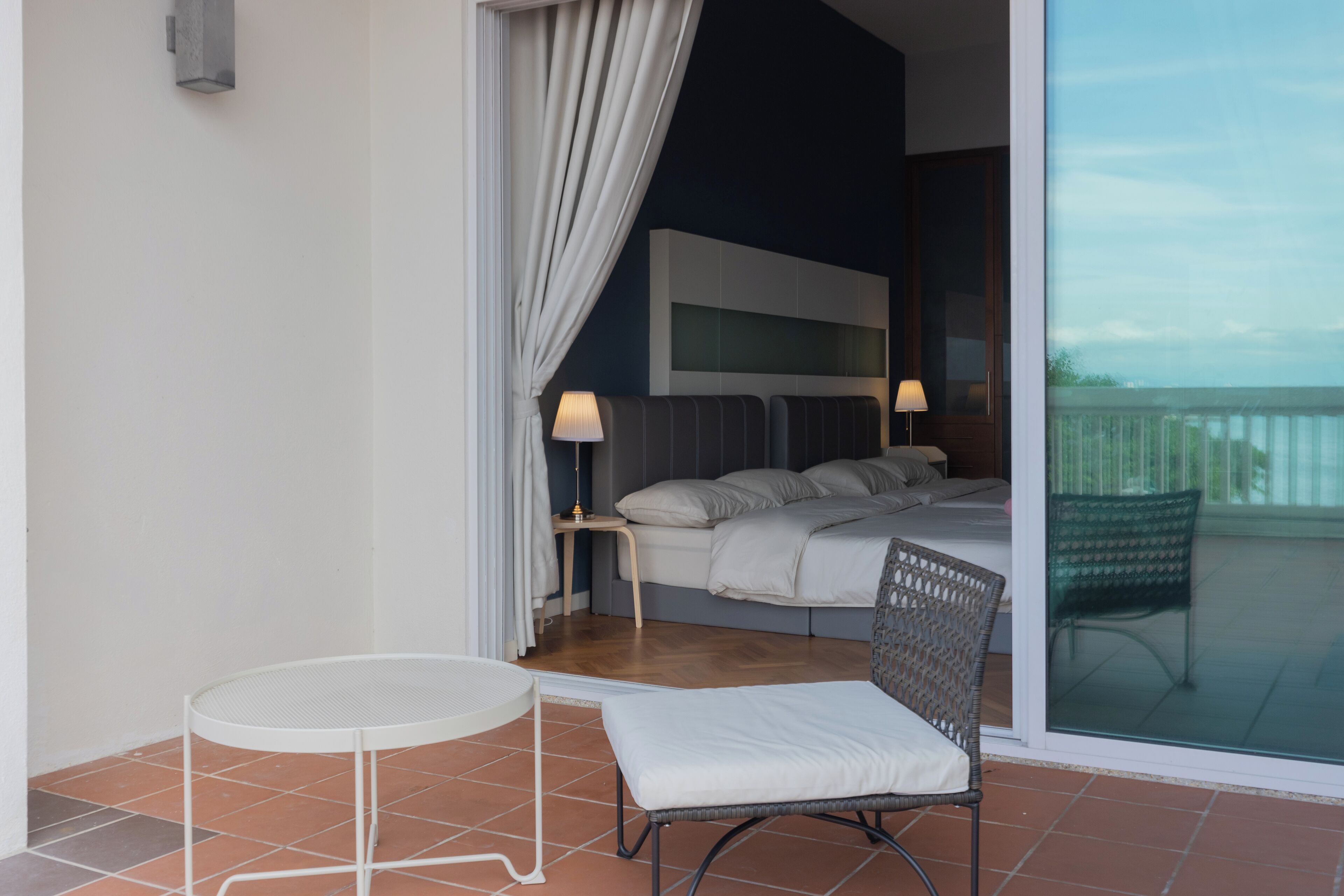 A modern bedroom with a bed, bedside lamps, a small round table, and a wicker chair.