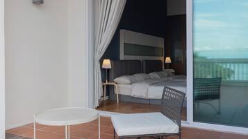 A modern bedroom with a bed, bedside lamps, a small round table, and a wicker chair.