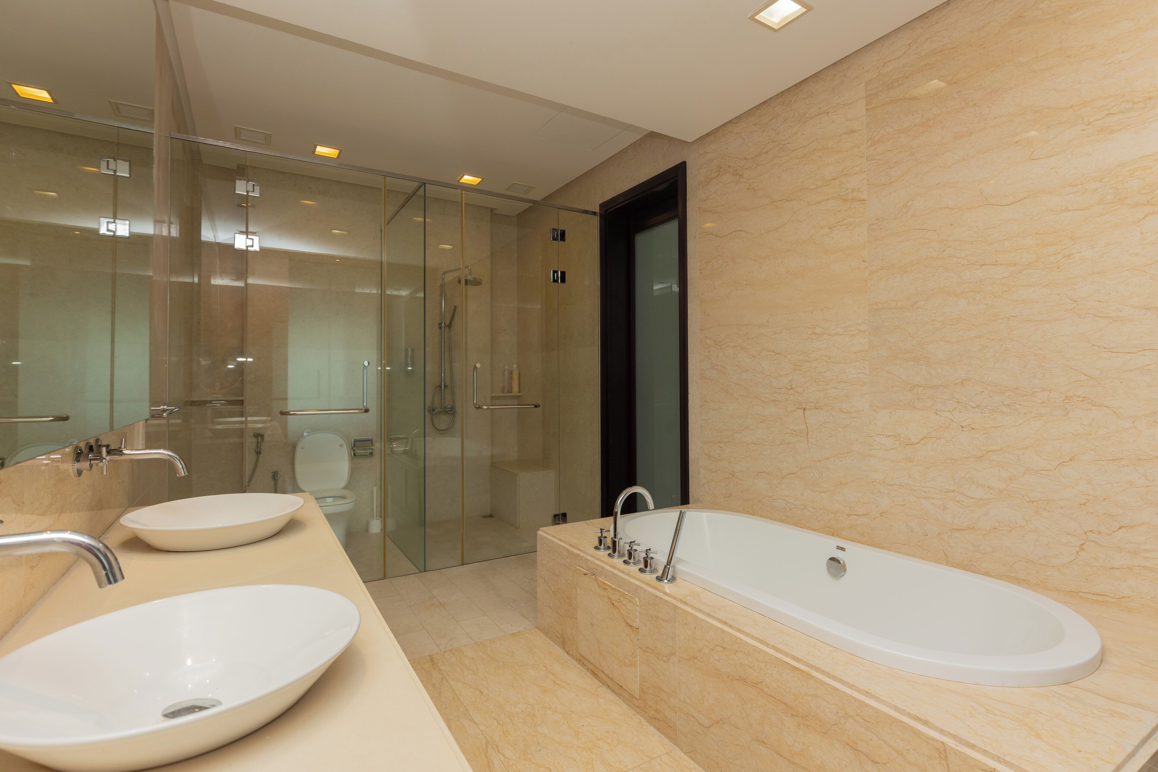 A modern bathroom with a large bathtub, two sinks, a glass shower enclosure, and a marble wall.