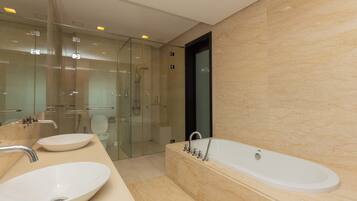 A modern bathroom with a large bathtub, two sinks, a glass shower enclosure, and a marble wall.