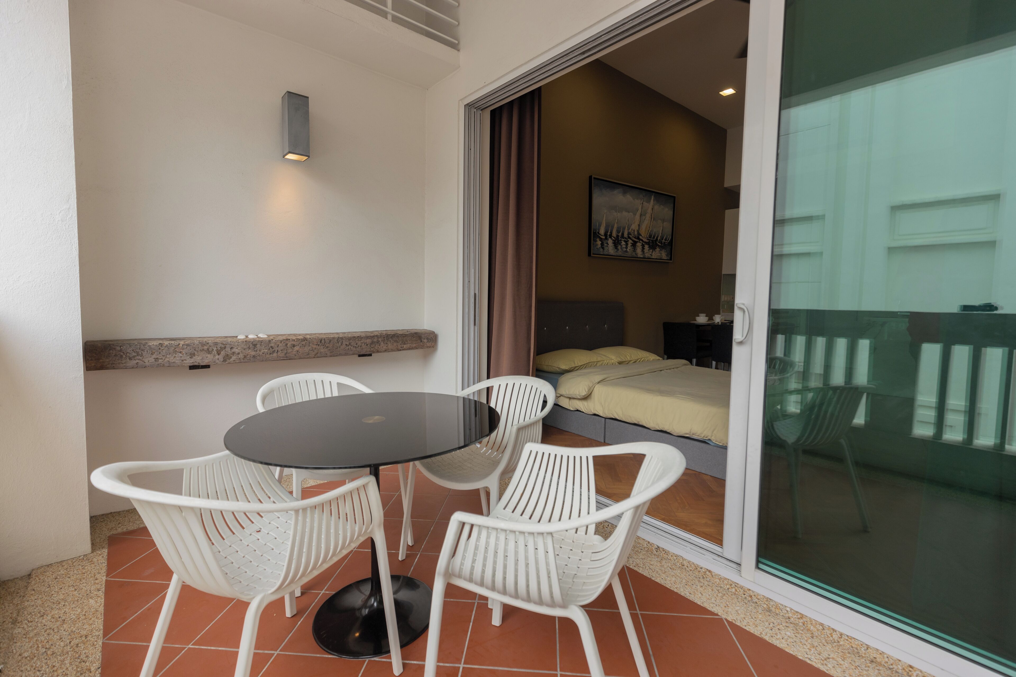 Een balkon met een tafel, stoelen, een bed en een schilderij aan de muur.