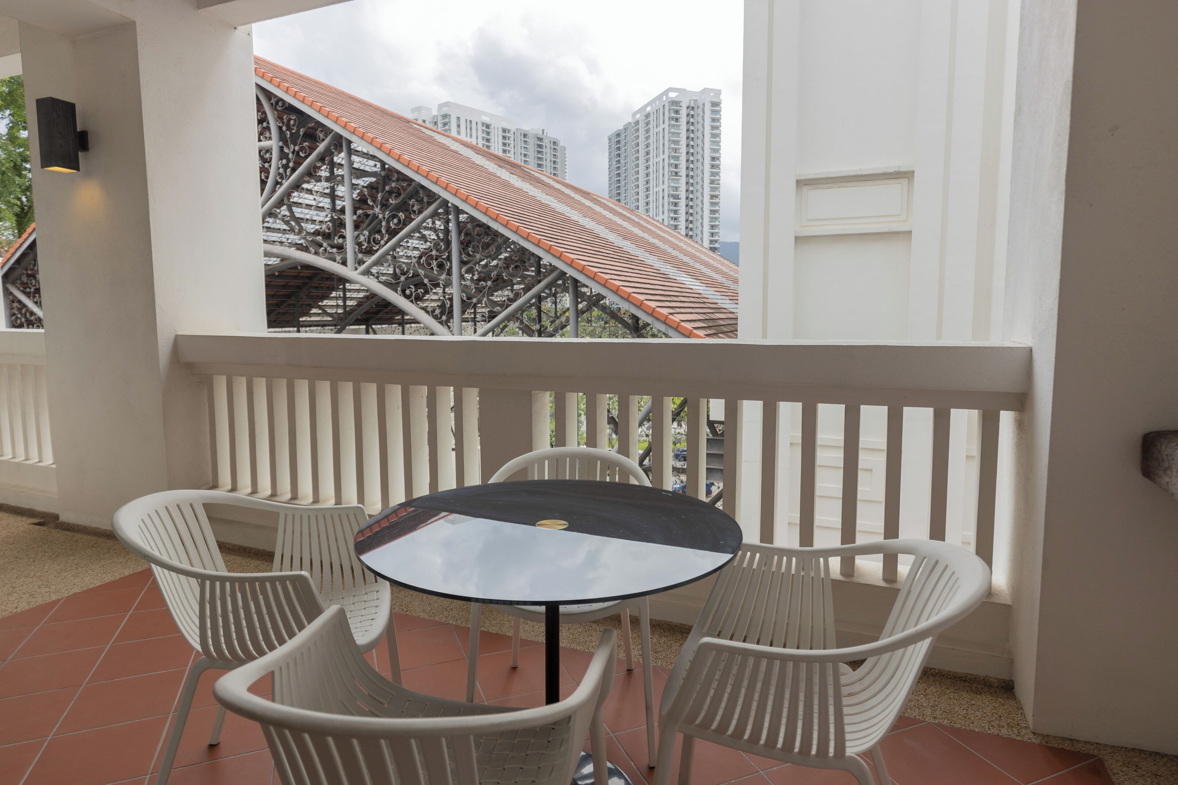 Un balcón con mesa y sillas, con vista a una escalera metálica y edificios altos.