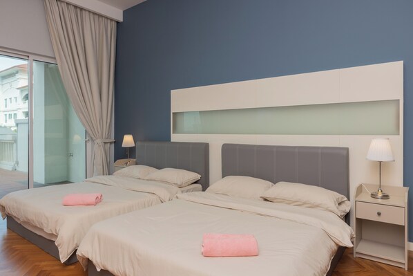 A hotel room with two beds, a large window with curtains, a nightstand with a lamp, and a view of buildings outside.