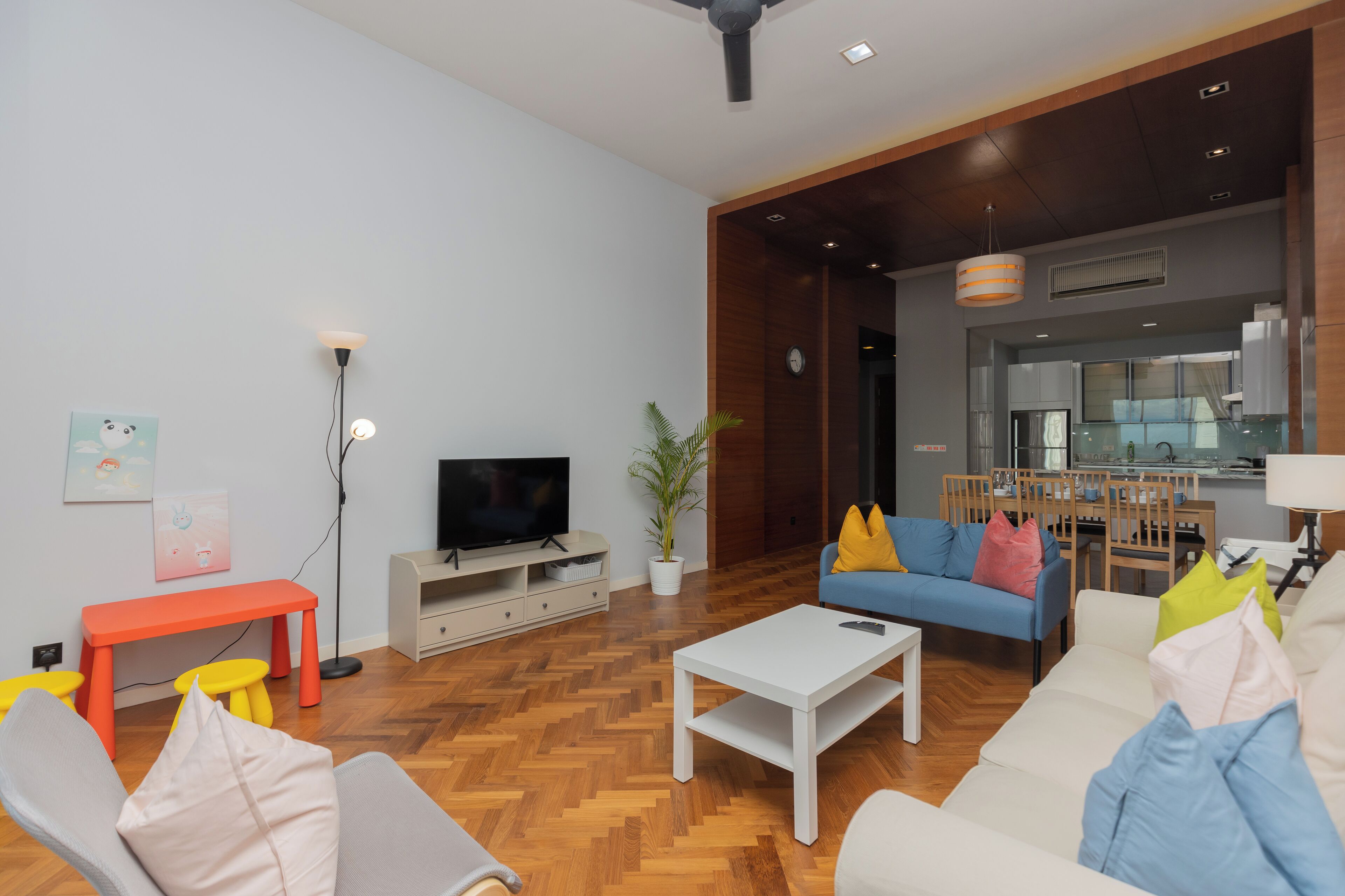 Een moderne woonkamer met een flatscreen televisie, een witte salontafel en een blauwe bank met kleurrijke kussens.