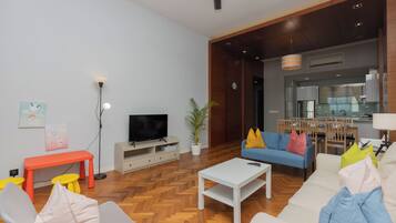 Een moderne woonkamer met een flatscreen televisie, een witte salontafel en een blauwe bank met kleurrijke kussens.