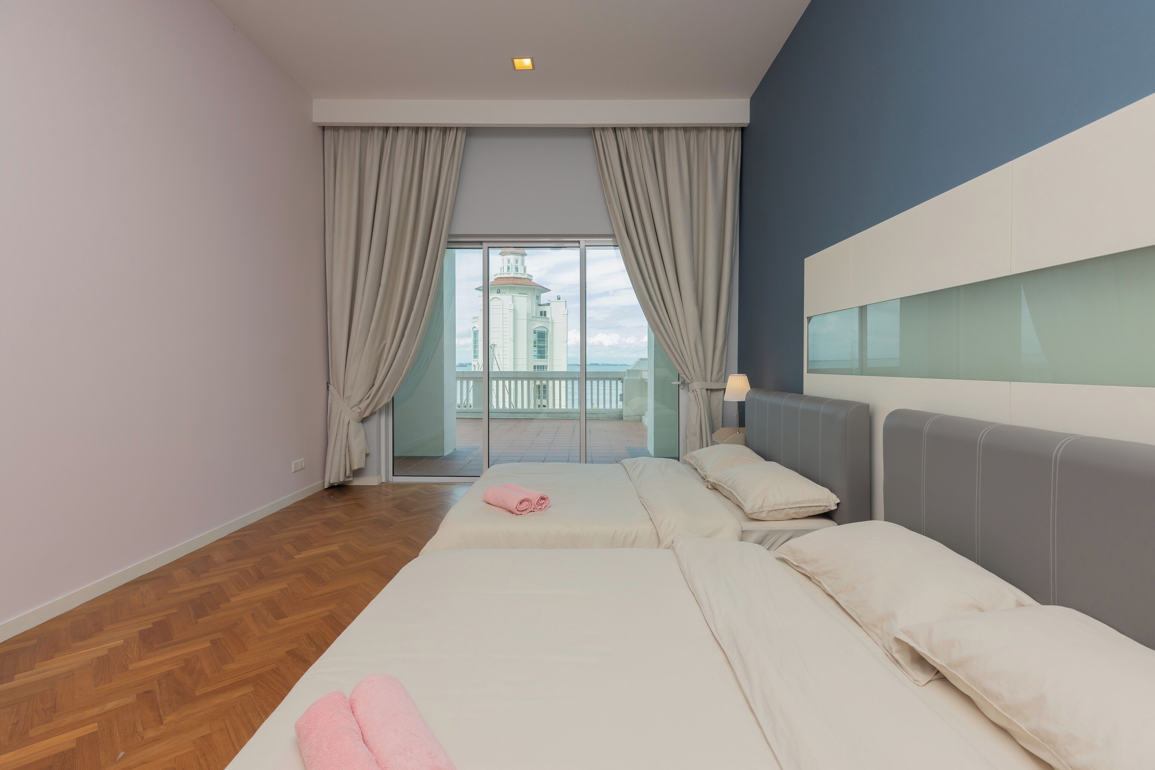 A hotel room with two beds, a balcony with a view of a building, and a wooden floor.