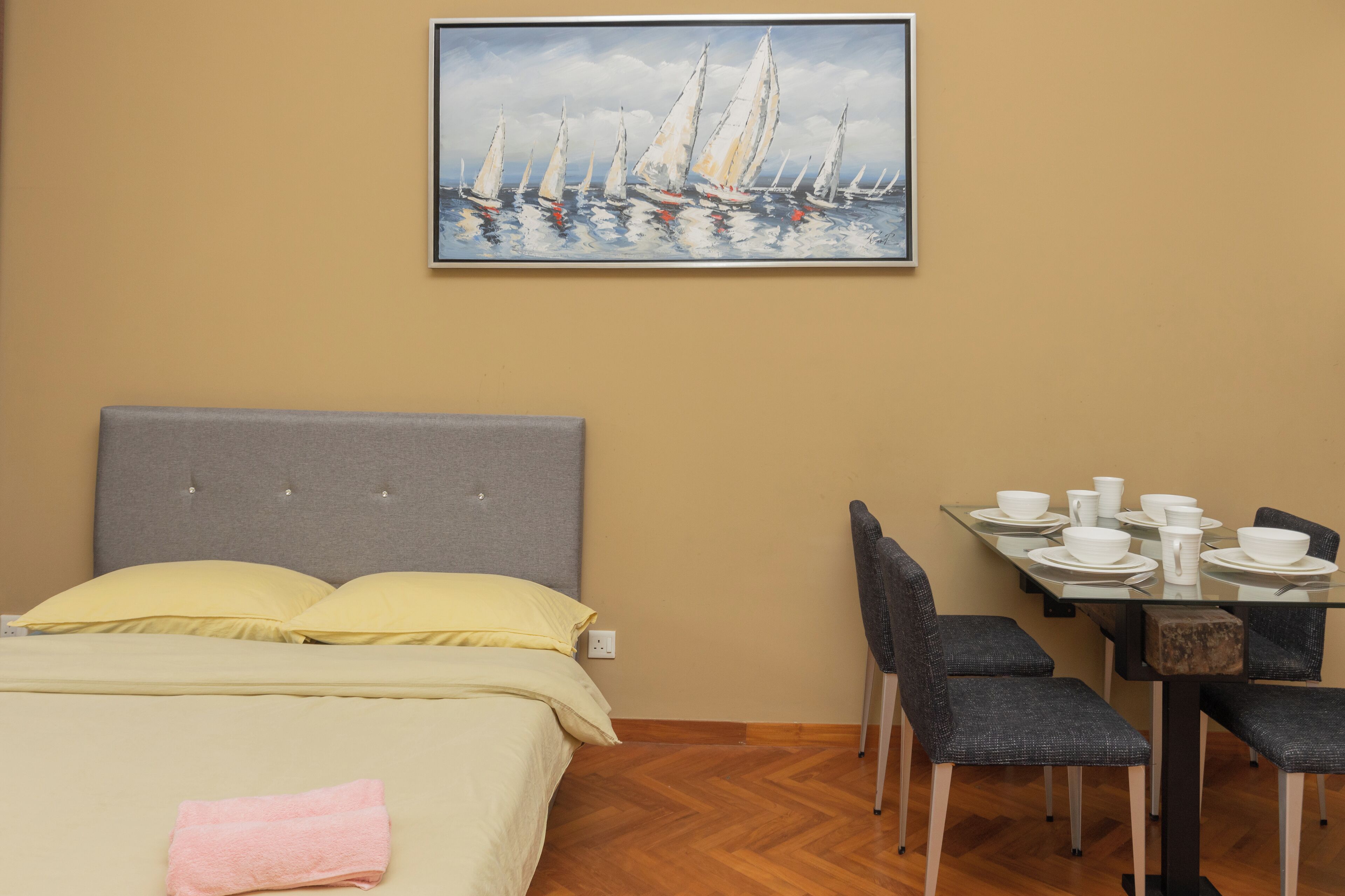 Habitación de hotel con una cama, una mesa de comedor con vajilla blanca y un cuadro de veleros en la pared.