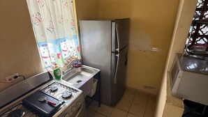 Cocina compacta con estufa a gas, refrigerador y ventana con cortina.