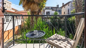 Un balcon avec une table ronde, un fauteuil confortable et une vue sur les bâtiments et la verdure.