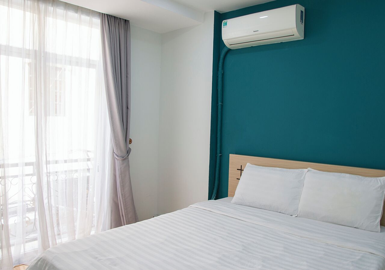 Ein Hotelzimmer mit einem Bett, weißen Leinen, einer türkis farbenen Akzentwand und einer Klimaanlage.
